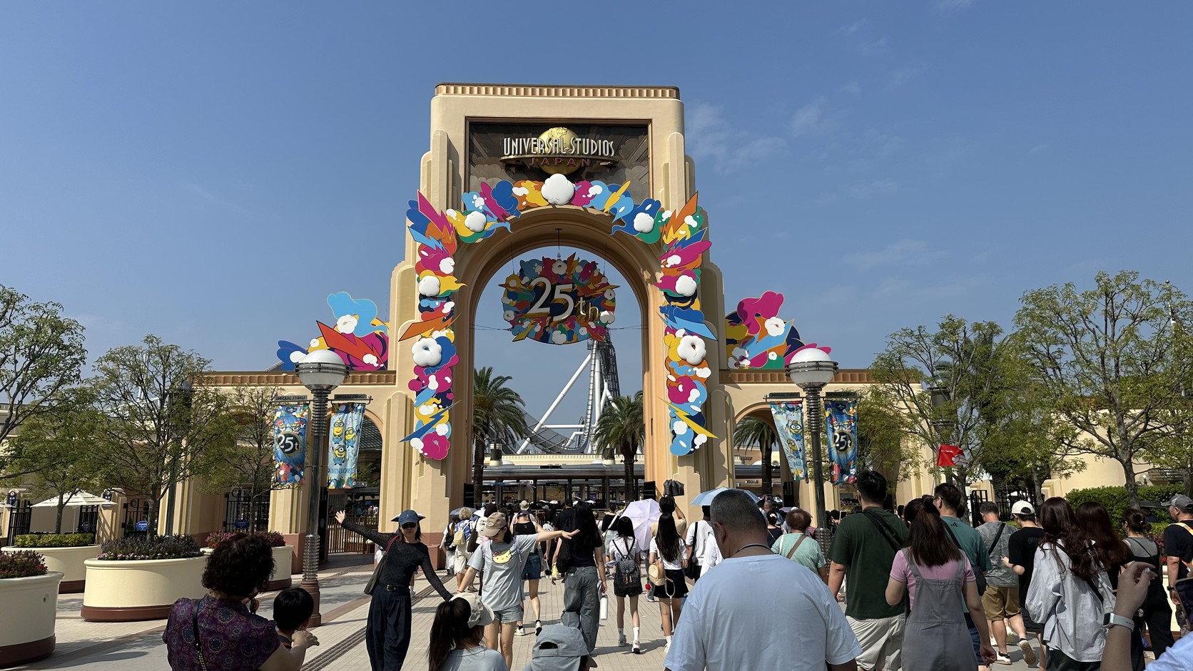 掛著 25 週年裝飾的園區入口拱門，前方是進場的遊客