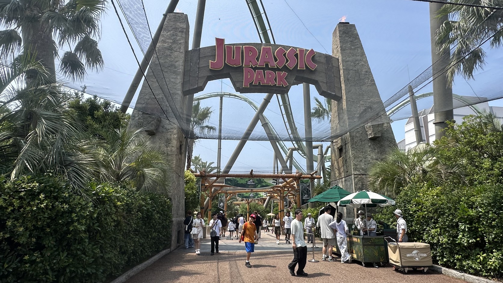 侏羅紀公園入口的 JURASSIC PARK 拱門，後方可見雲霄飛車軌道