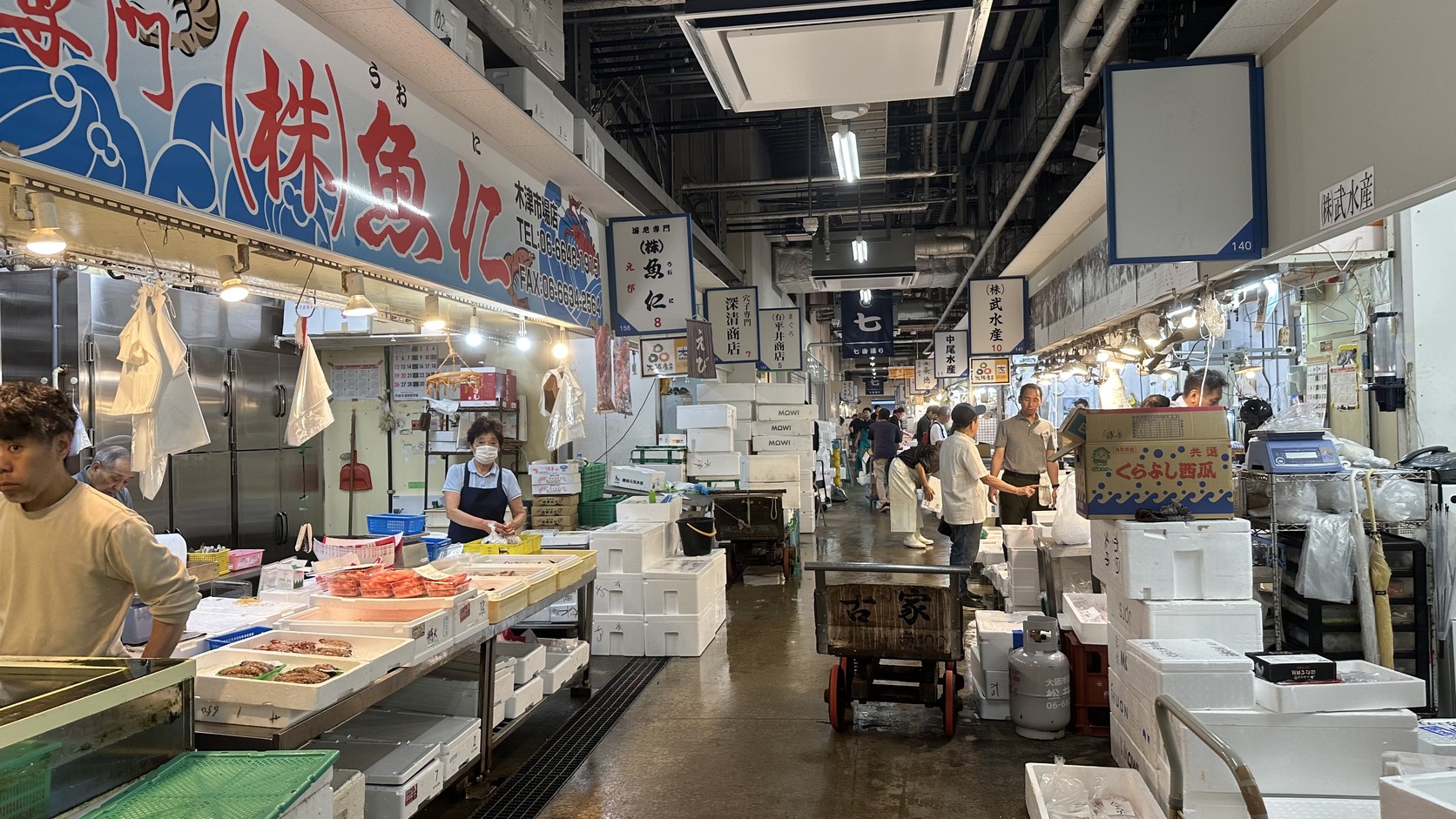 市場內的通道，兩側店家在整理貨物，地面濕潤並堆放著保麗龍箱