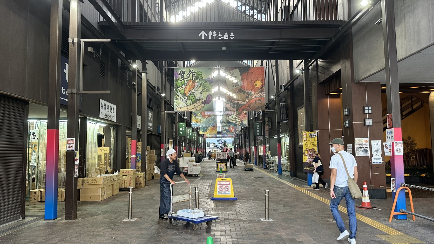 清晨的市場主通道，店員推著載有保麗龍箱的推車，旁邊有人走過