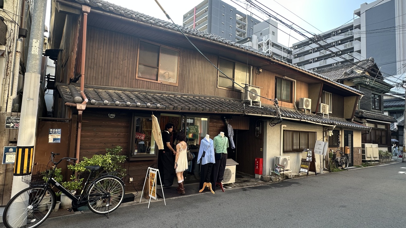 木造老屋一樓的古著店，衣服掛在木造門窗前並立著人台