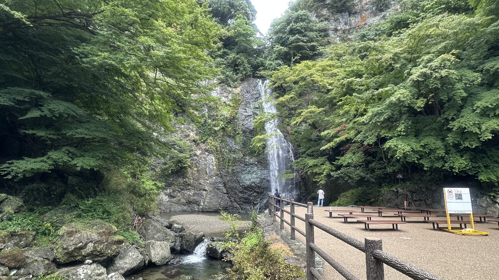箕面大瀑布遠景，前方是設有木製長椅與欄杆的休憩區
