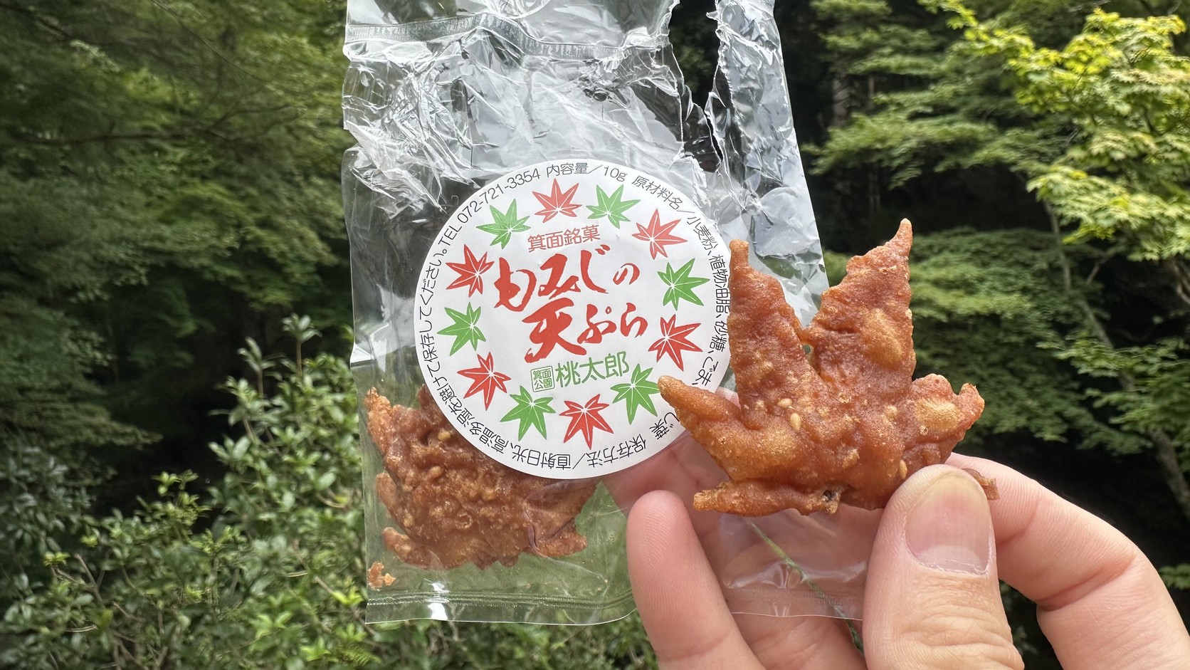手拿一包桃太郎的「もみじの天ぷら」袋裝紅葉天婦羅與一片楓葉形的天婦羅