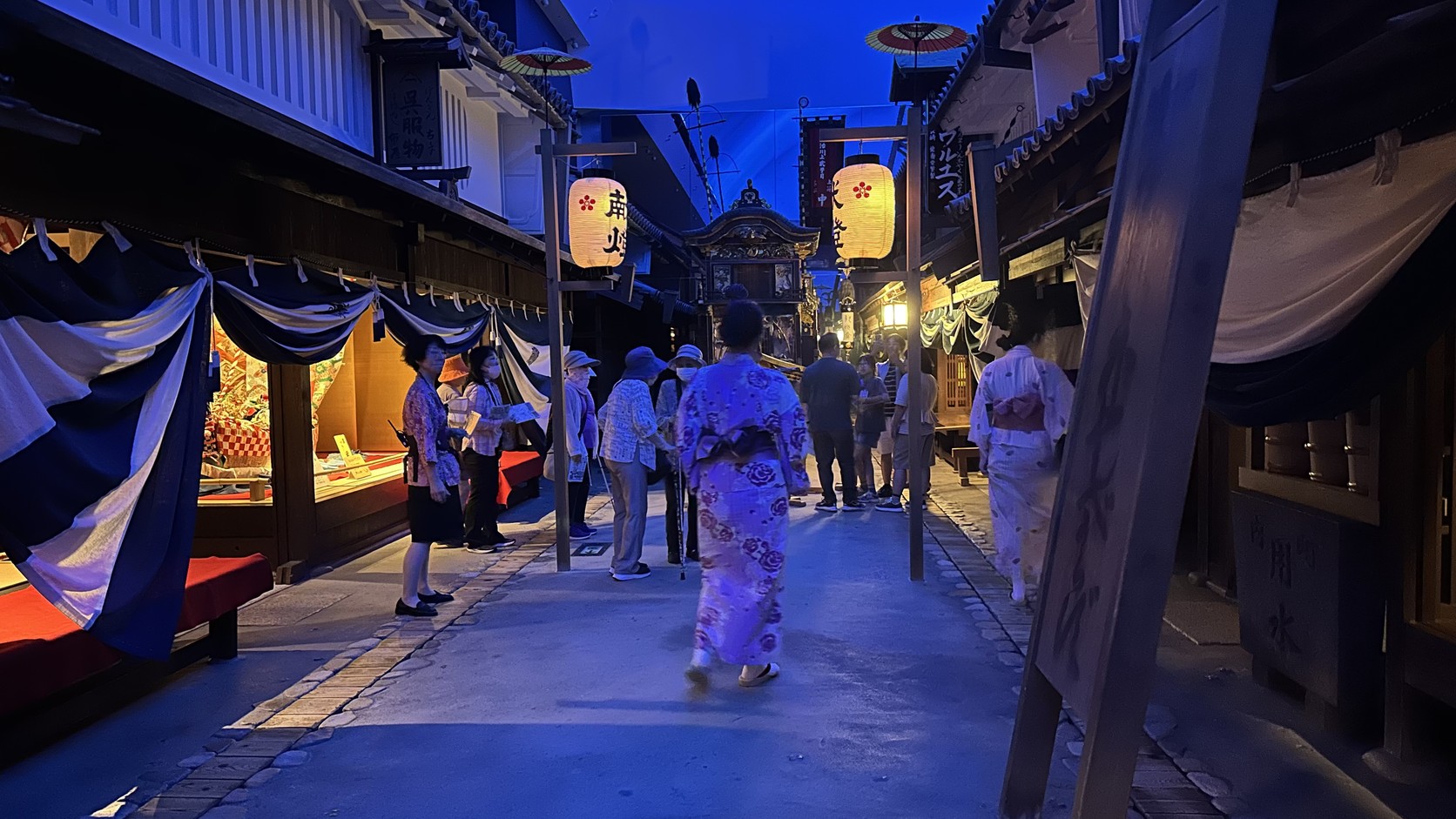 夏祭夜晚的街道，成排獻燈燈籠亮起，遊客穿著浴衣走動