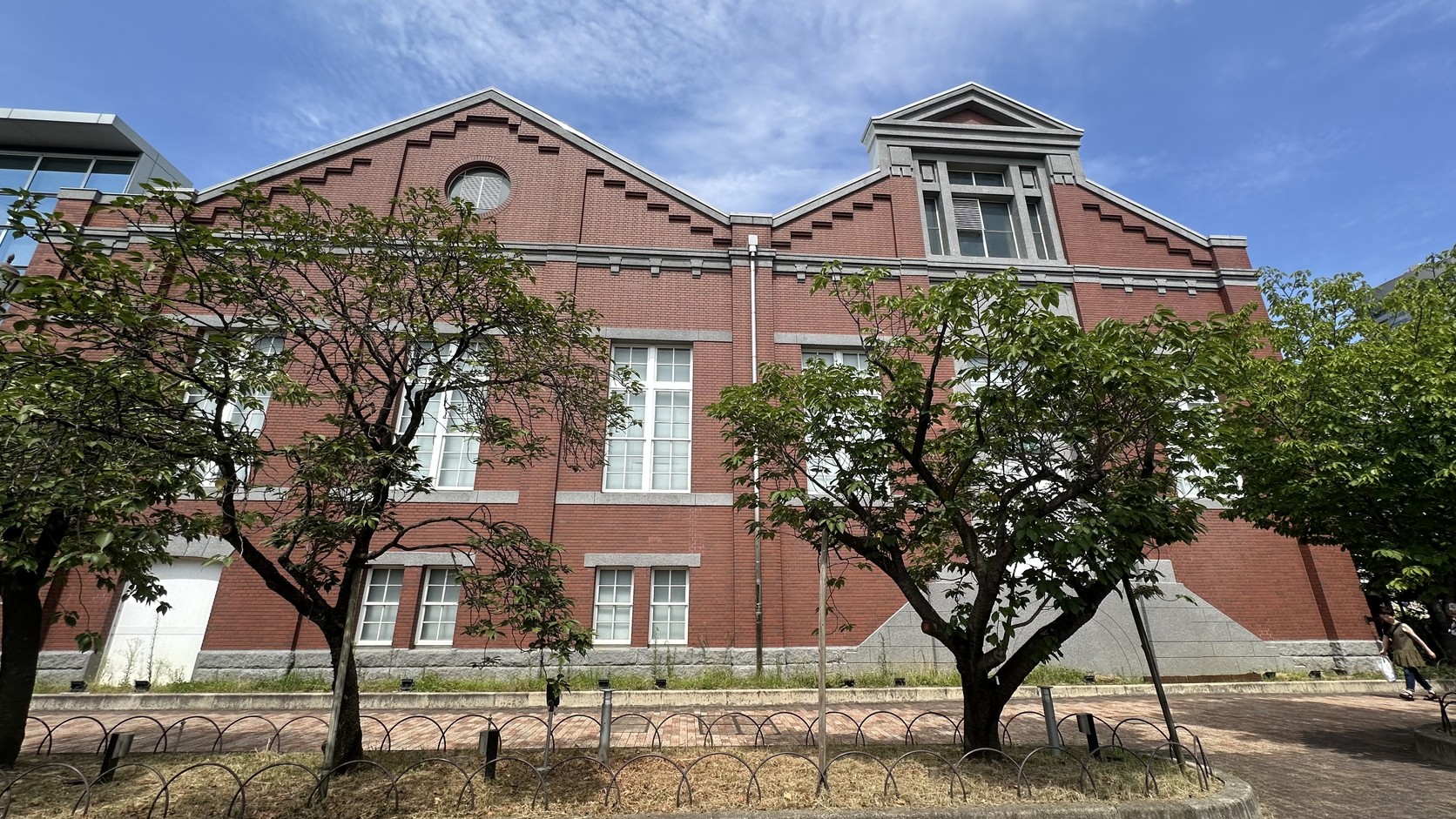 造幣博物館紅磚建築側面實拍：山形屋頂、灰色石材飾帶與前方櫻樹