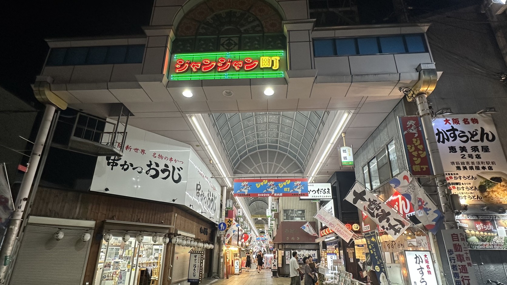 大阪新世界鏘鏘橫丁入口，拱門上亮著綠色「ジャンジャン町」霓虹燈