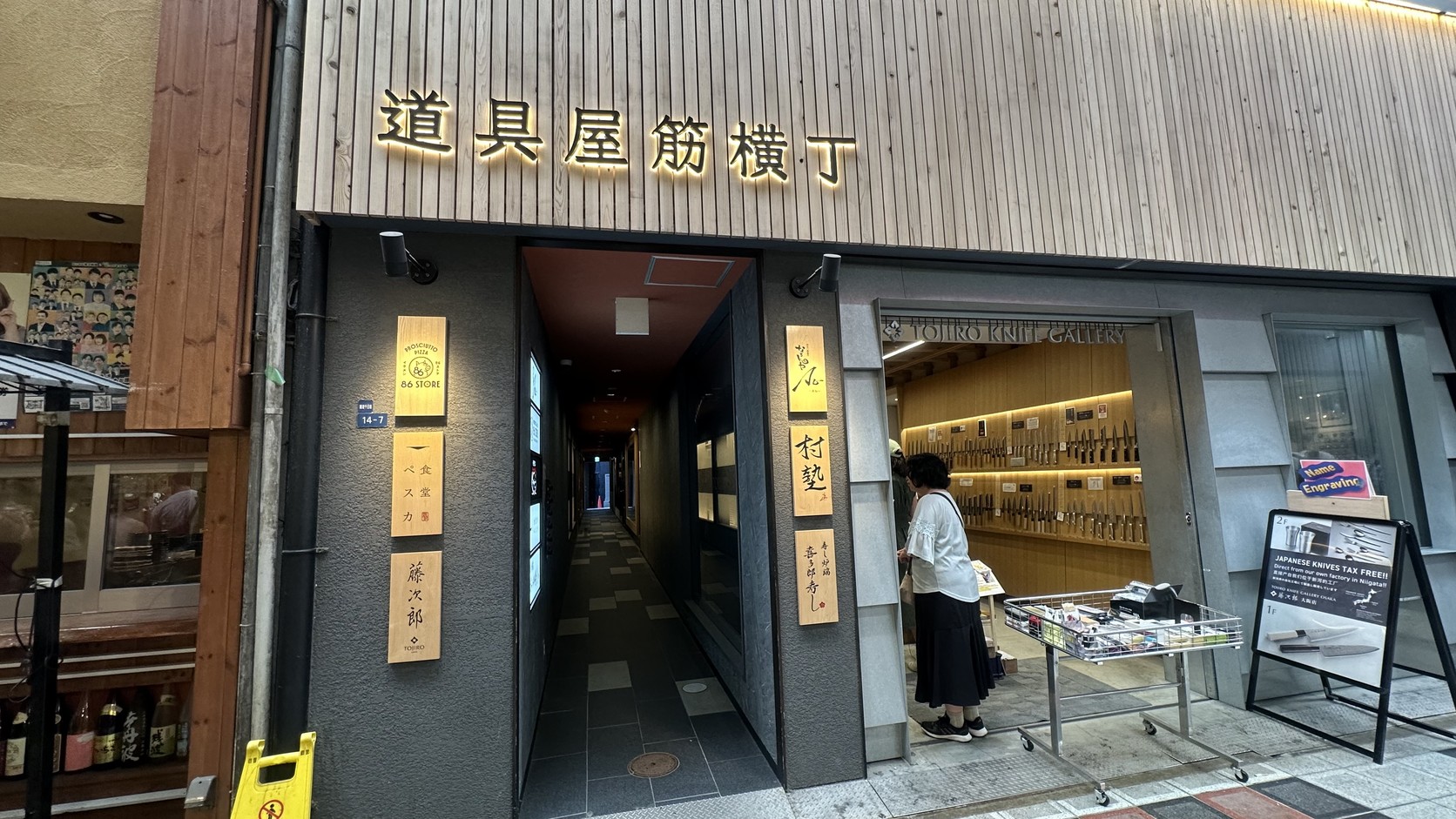 掛著「道具屋筋横丁」招牌的建築入口，一條細長通道往內延伸，旁邊店面陳列著刀具