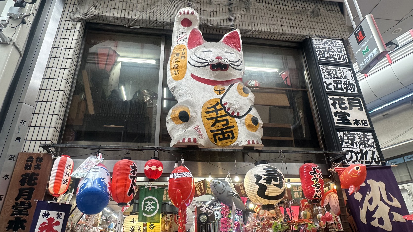 商店街店面上方的巨大招財貓，身上掛著寫有「千万両」的金牌，店名為花月堂本店