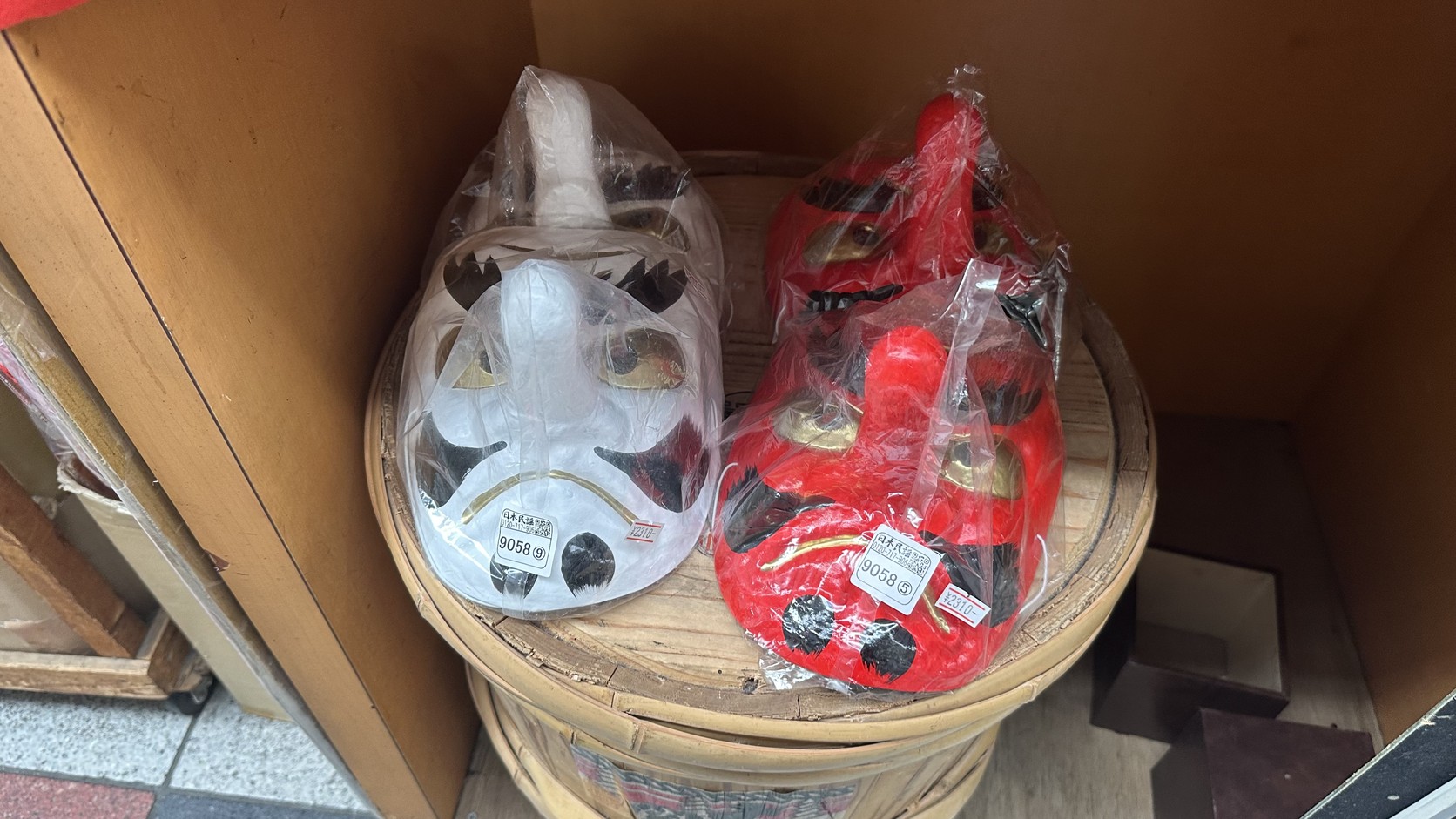 紅色與白色的天狗面具，以塑膠袋包裝陳列在竹籠上