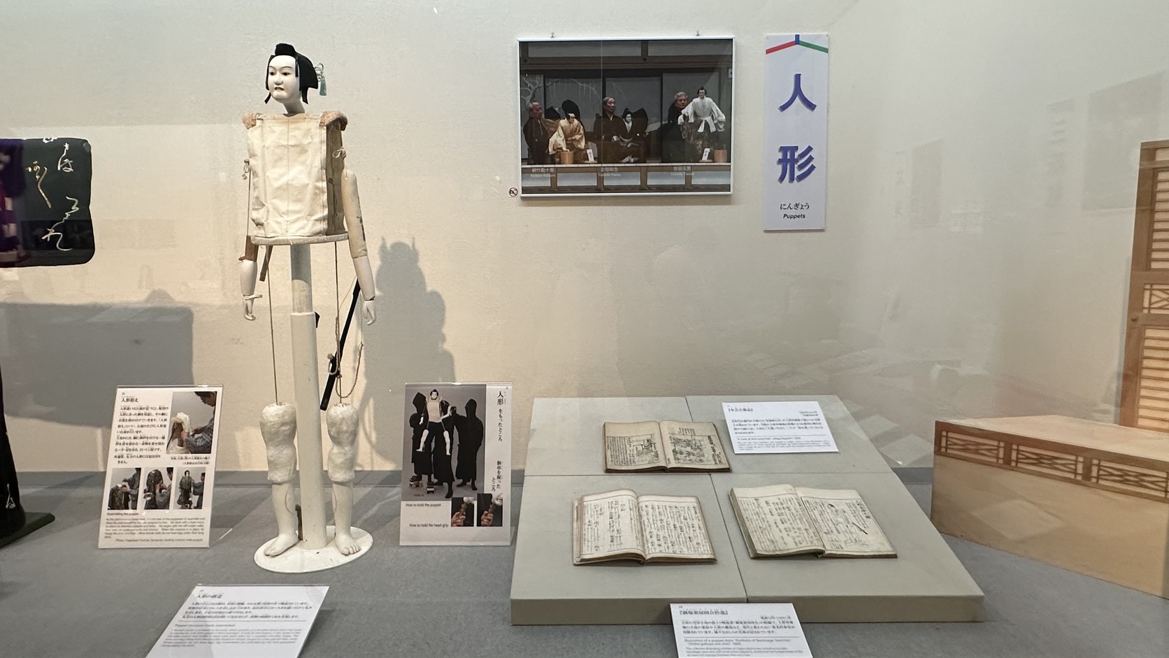 展示區的文樂人偶骨架：頭、肩板、竹製腰輪與繩線，旁邊展示古書與人形遣劇照
