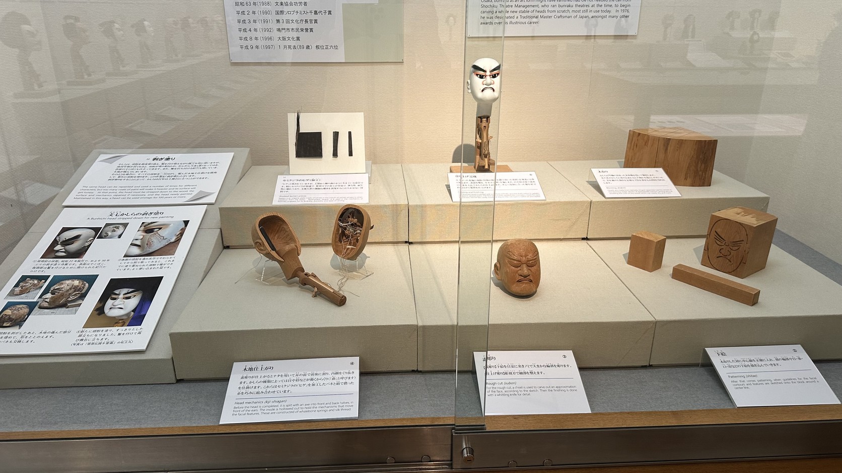 人偶頭的製作工序展示：原木、下繪、荒彫り、木地仕上がり，以及以鯨鬚彈簧和絲線構成的內部機關