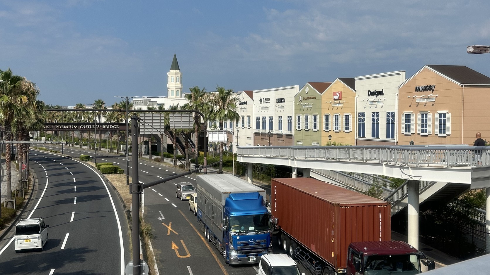天橋上看到的臨空 Premium Outlets 鐘塔與歐式建築街區，道路上有貨櫃車