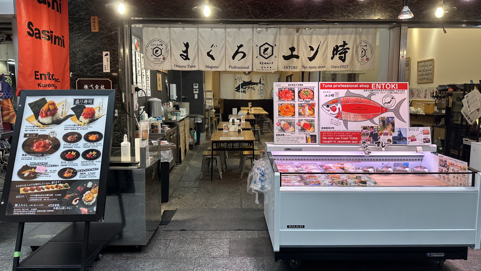 ENTOKI（まぐろのエン時）黑門市場本店店面，掛著暖簾與菜單立牌，門口有鮪魚冷藏展示櫃，店內座位區已點亮