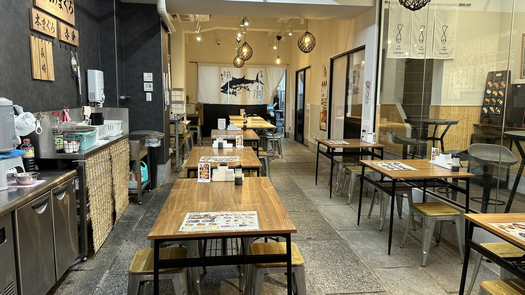 ENTOKI 店內座位區，長方形木桌與高腳椅，牆面有「本日のまぐろ」黑板，桌上放著圖片菜單