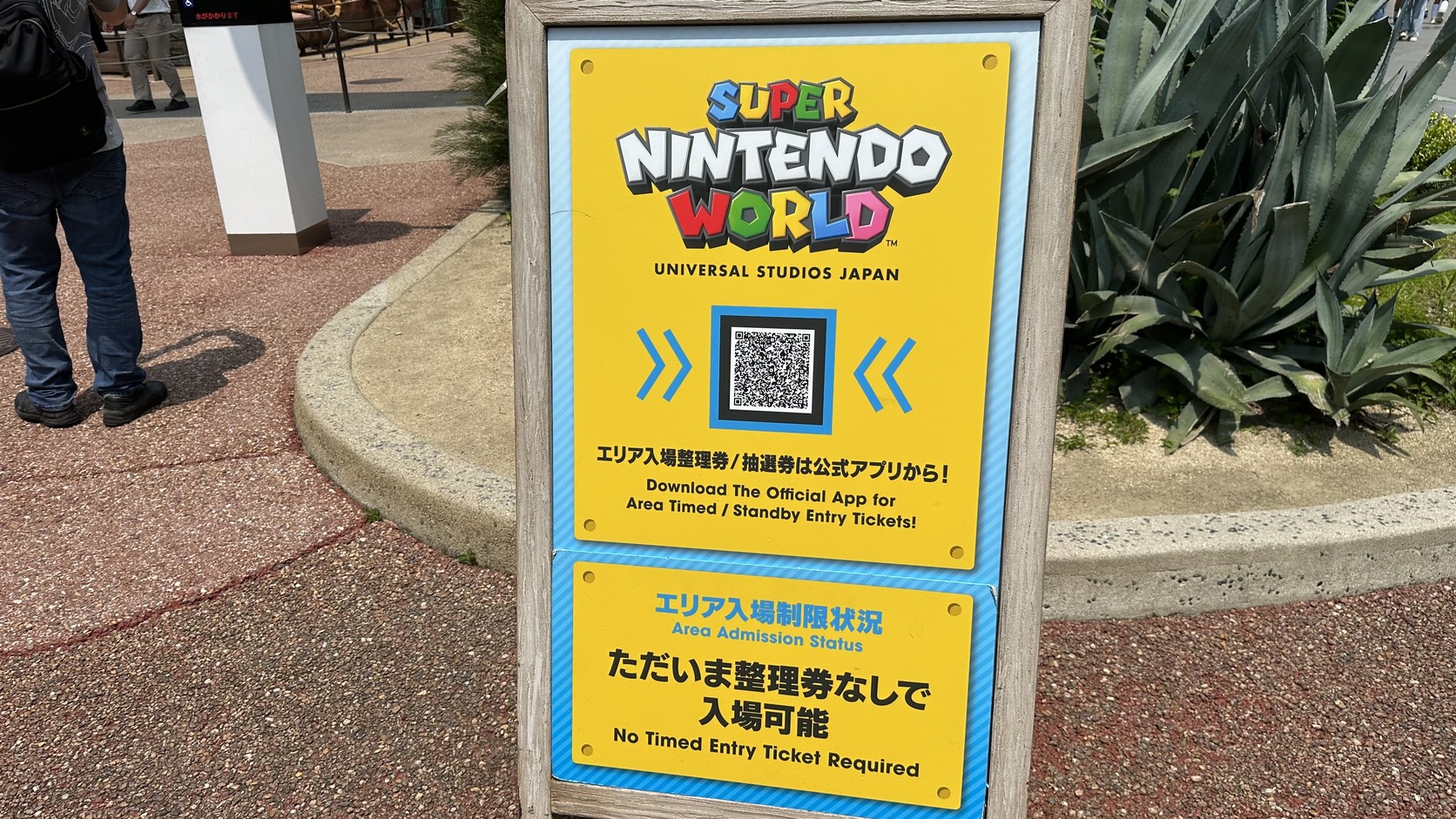 超級任天堂世界入口立牌：上方有官方 App 的 QR Code，黃底告示寫著「ただいま整理券なしで入場可能」與 No Timed Entry Ticket Required