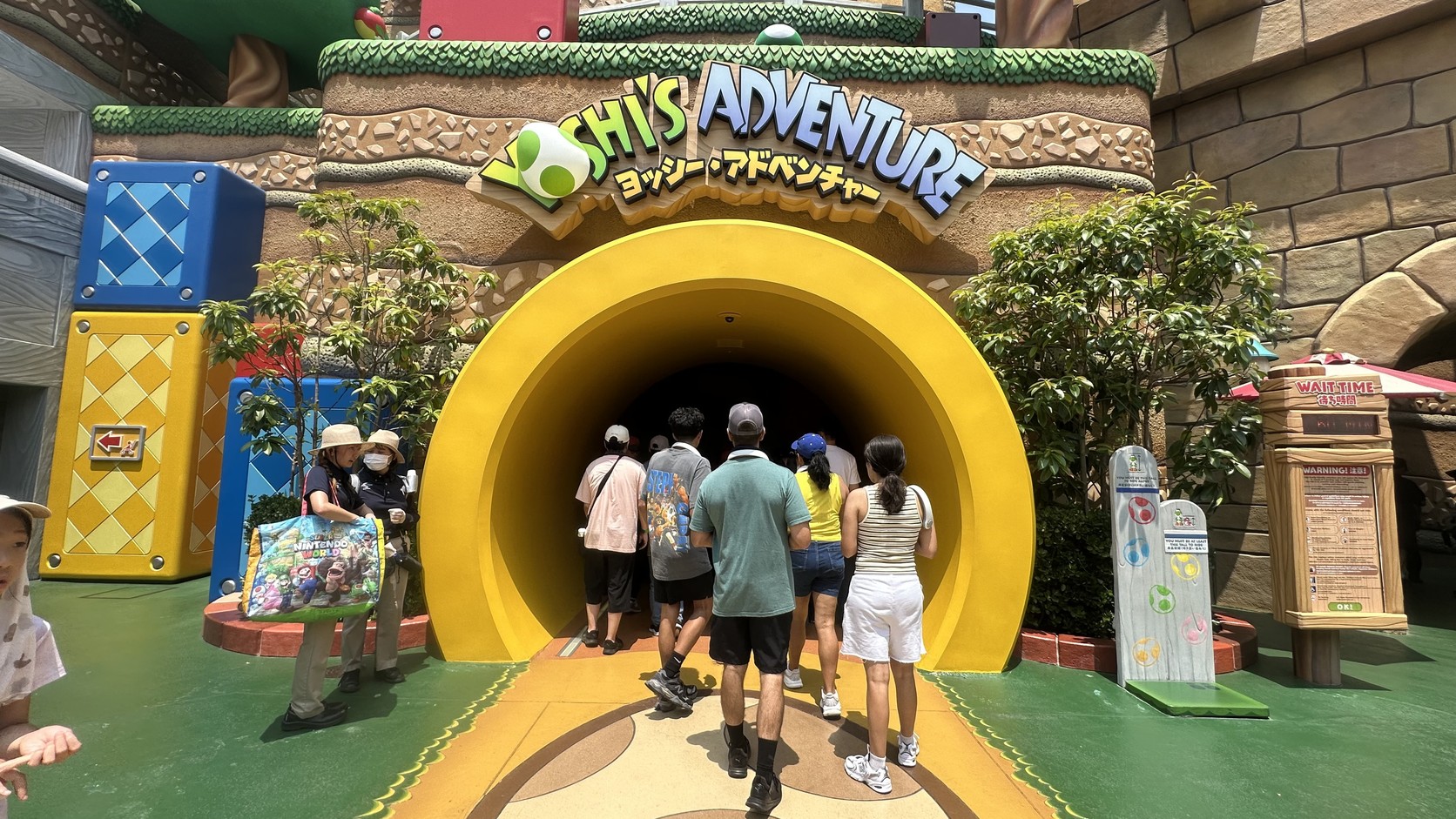 耀西冒險的入口：黃色圓形隧道，上方招牌寫著 YOSHI'S ADVENTURE，遊客正排隊走進去