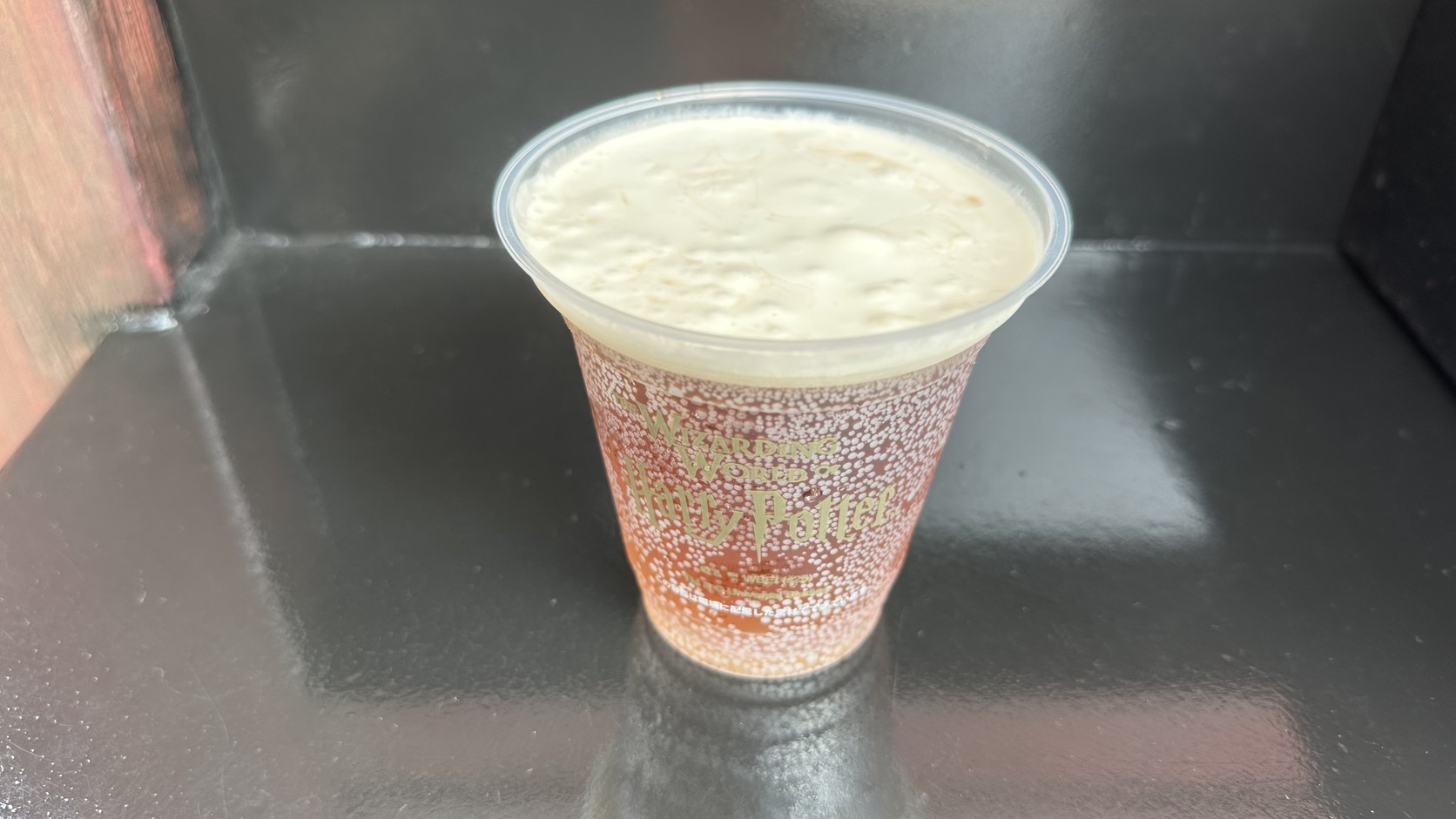 一杯奶油啤酒：透明塑膠杯上印著園區標誌，杯中上層是厚厚的白色奶泡