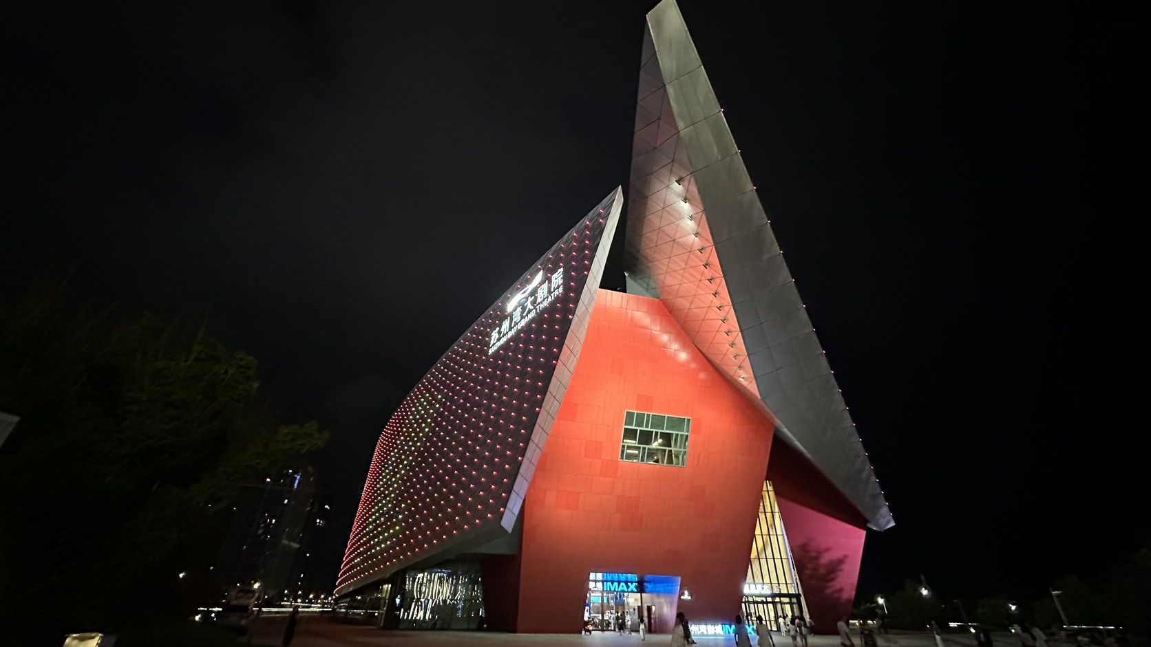 蘇州灣大劇院夜間外觀：紅色主體搭配兩片斜切的金屬屋頂，左側斜面亮著劇院名稱，入口處有 IMAX 招牌
