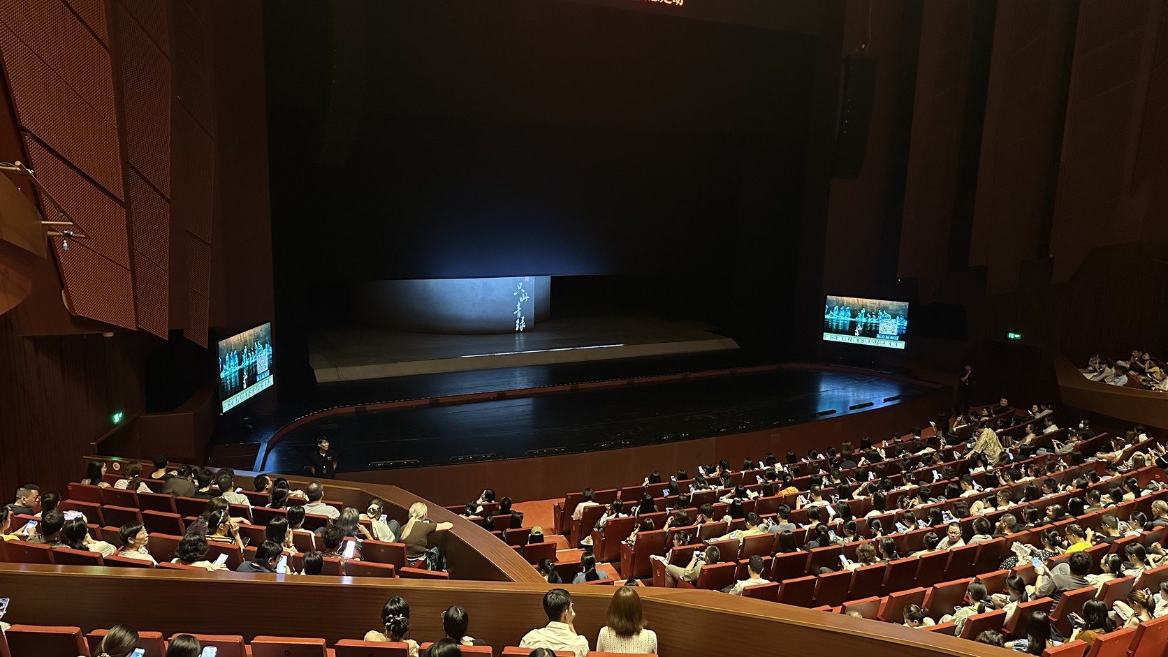 開演前的蘇州灣大劇院歌劇廳：舞台尚未開始演出，觀眾席滿座，舞台兩側的螢幕播放宣傳畫面