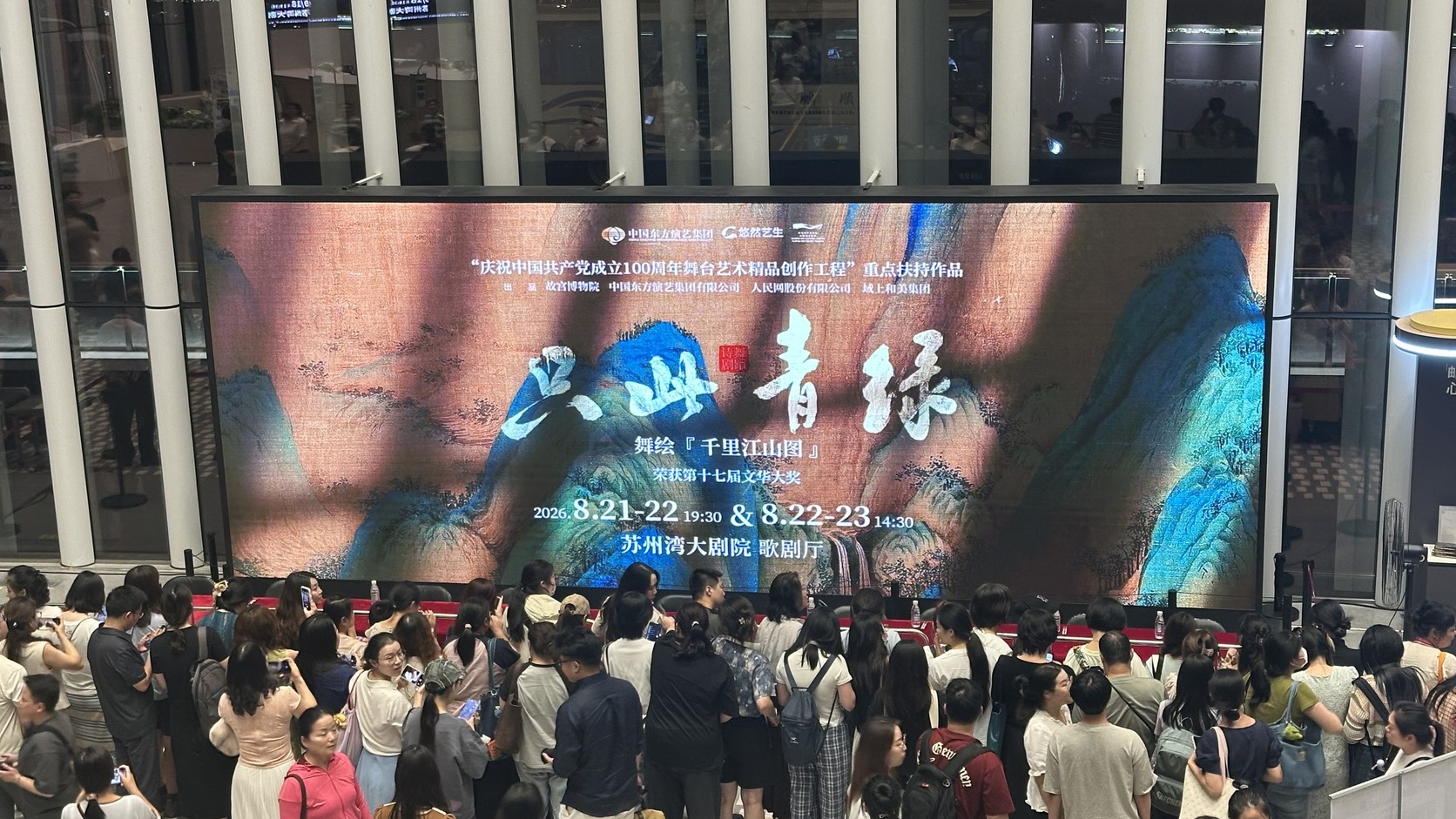 蘇州灣大劇院大廳的大型螢幕：播放《只此青綠》舞繪《千里江山圖》的演出日期與場地資訊，前方聚集拍照的觀眾