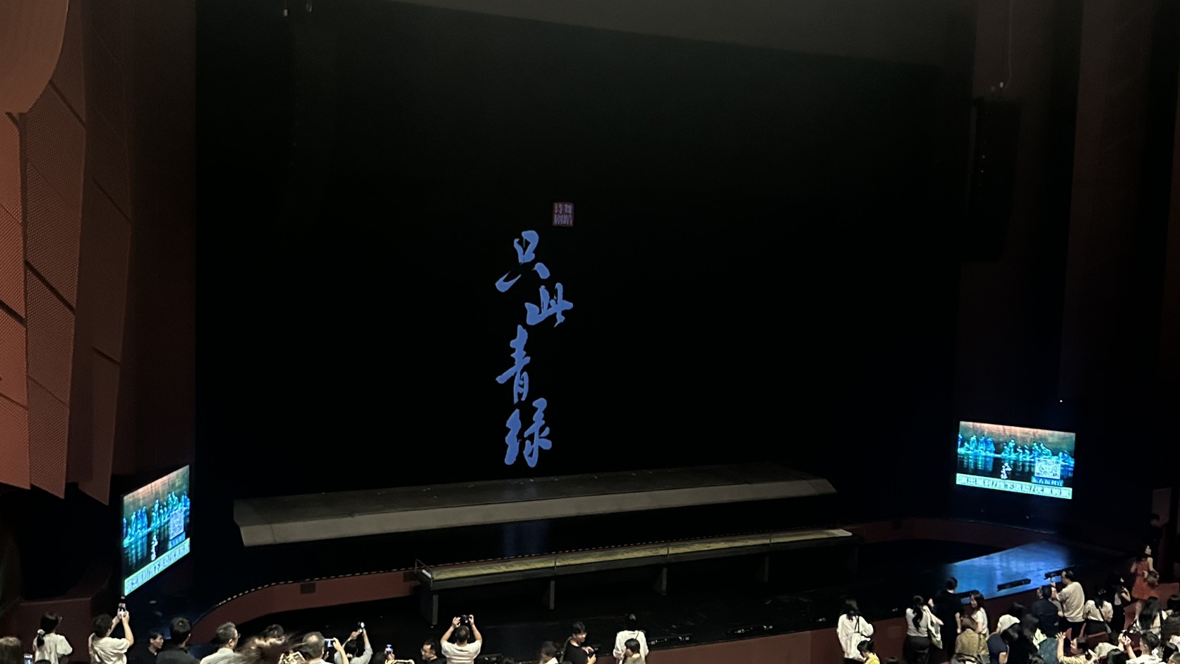 謝幕後的歌劇廳舞台：黑幕上亮起藍色書法《只此青綠》標題，舞台兩側有螢幕，前排觀眾舉起手機拍照