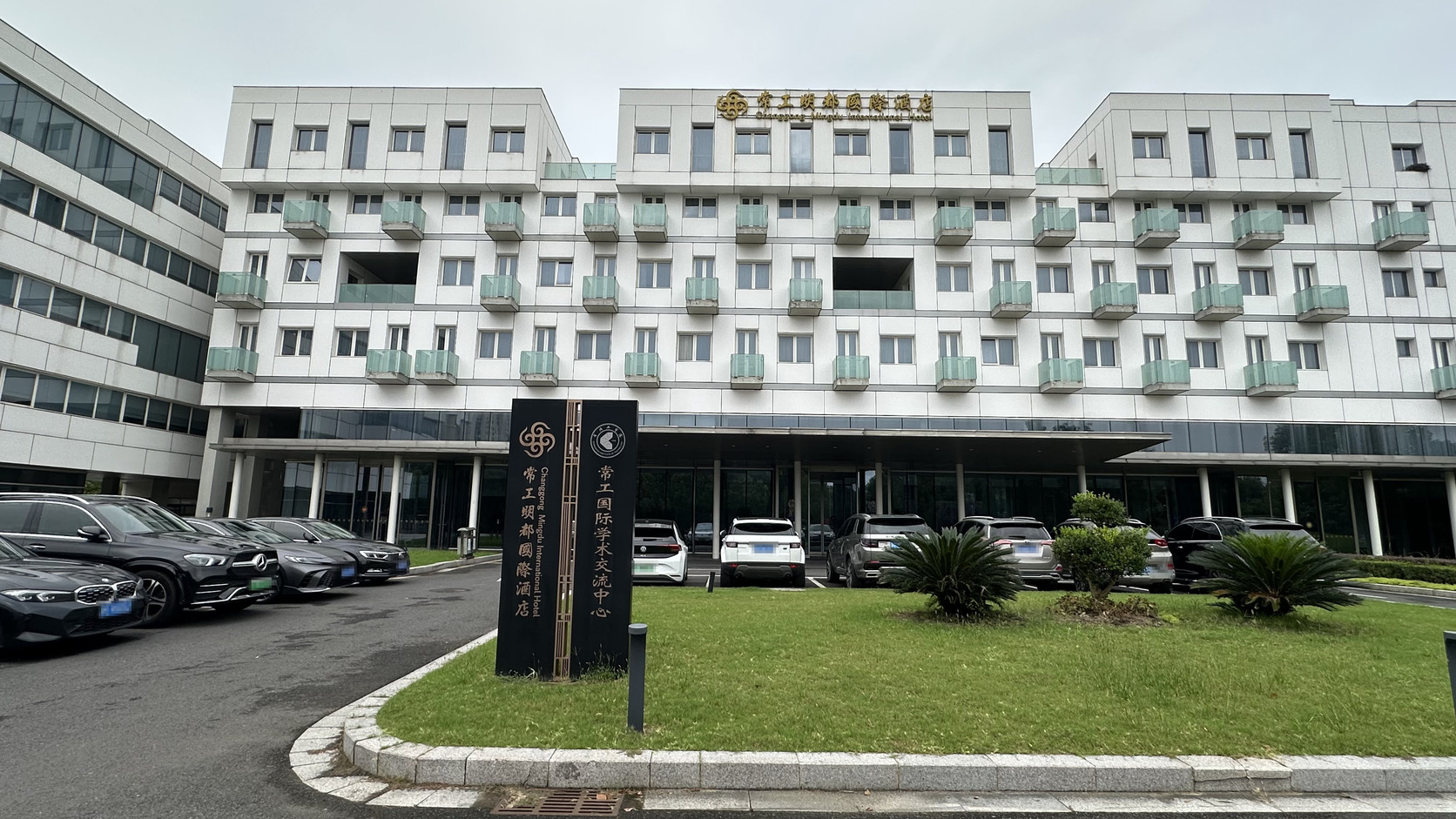 常工明都國際酒店白色外觀與草坪前的雙名稱立牌，立牌寫著「常工明都國際酒店」與「常工國際學術交流中心」