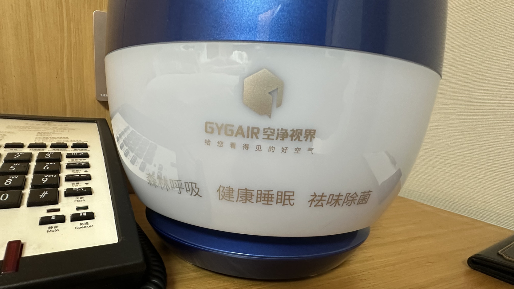 床頭櫃上的藍白色 GYGAIR 空氣淨化設備，機身印有「淨化呼吸 健康睡眠 祛味除菌」