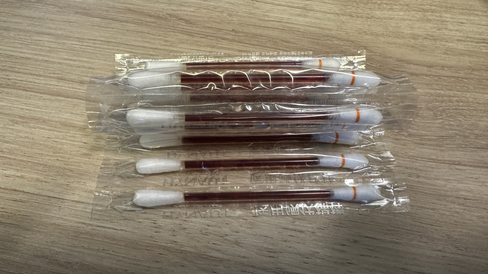獨立包裝的一次性棉棒，棒身內有深紅褐色液體，擺在木質桌面上