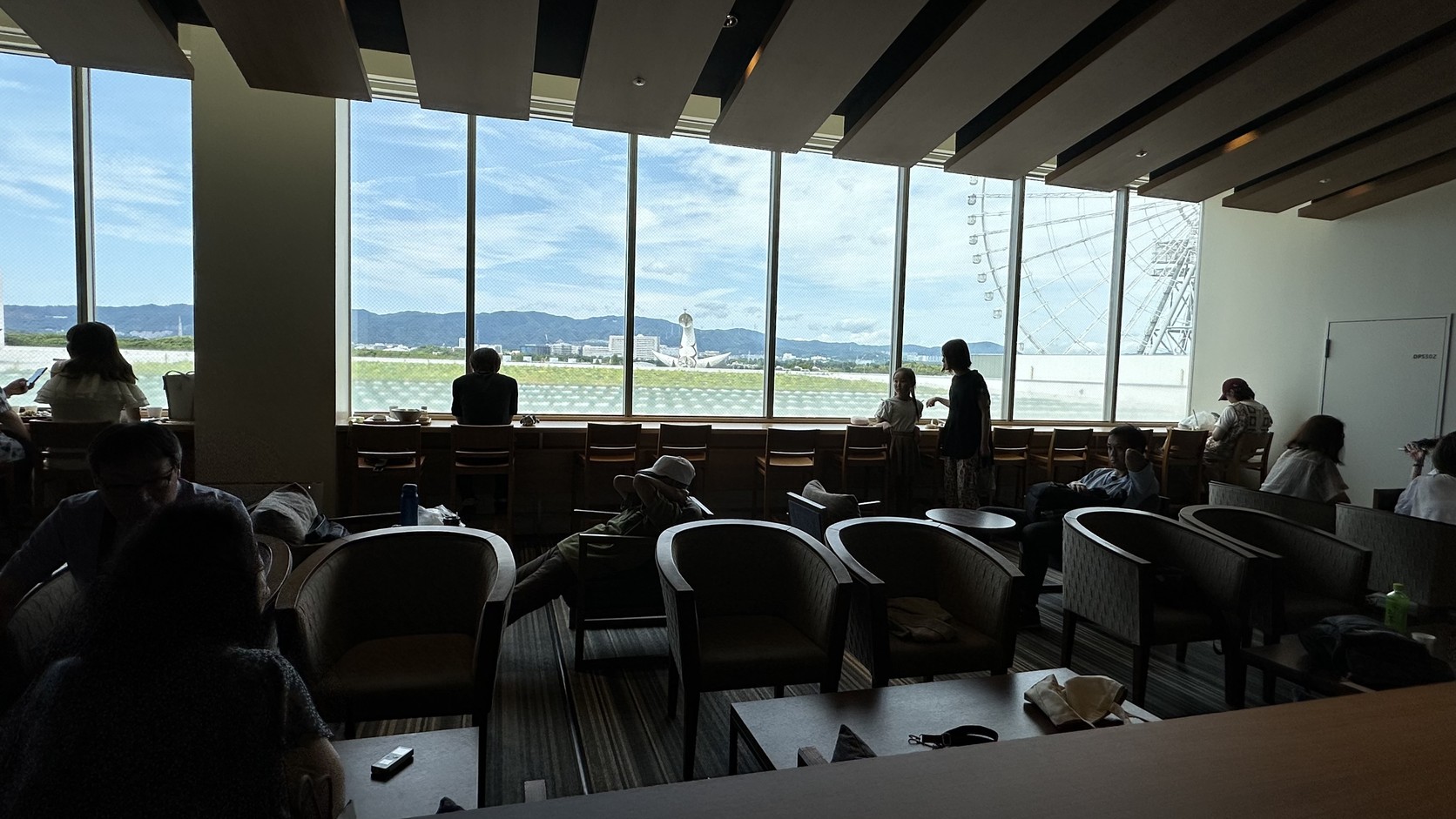 LaLaport窗邊的用餐與休息區，窗外遠處山景前是太陽之塔，右側是OSAKA WHEEL摩天輪