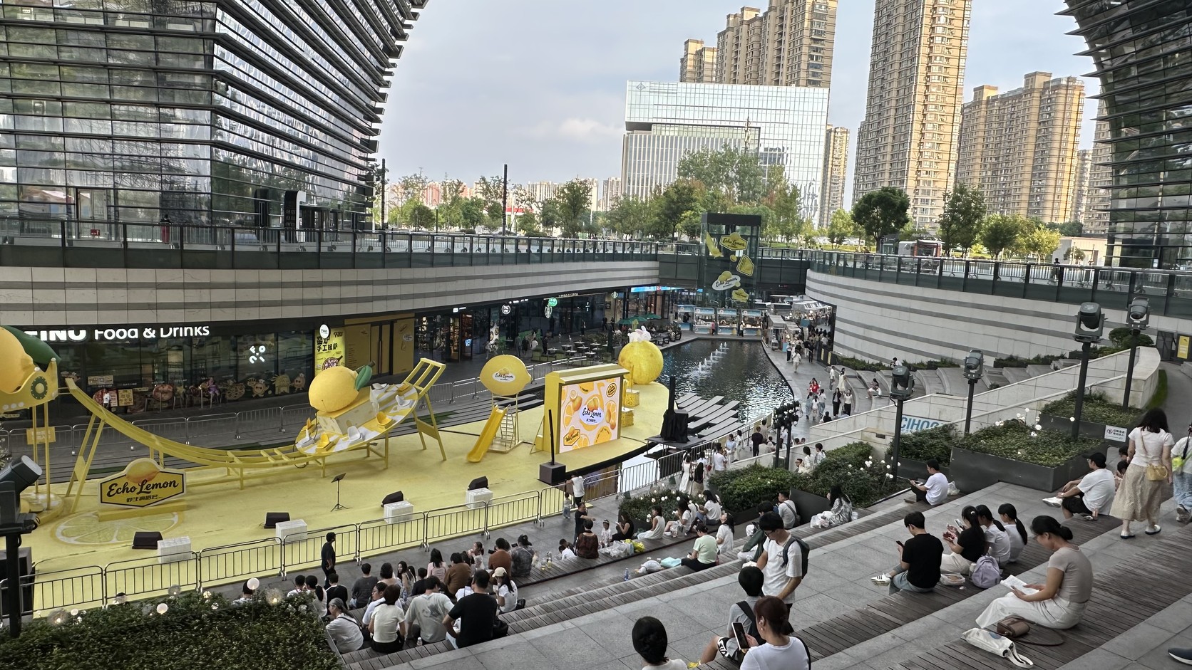 下沉廣場全景：水景、黃色舞台，以及階梯座席上等待演出的人群