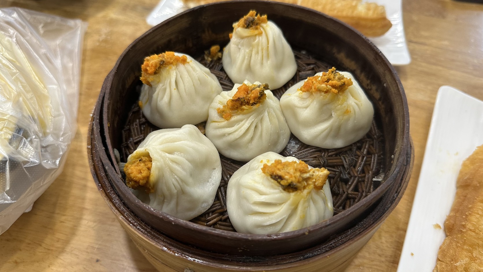 竹蒸籠中六顆小籠包，每顆頂端點綴橘黃色蟹黃