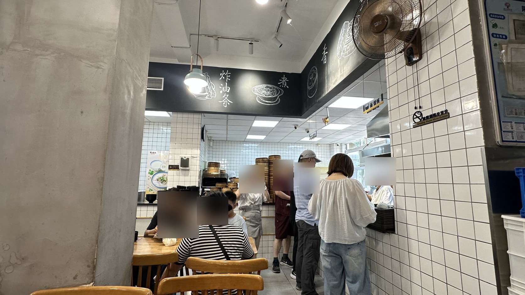 一樓用餐現場，牆面寫著炸油條與煮，客人在製作區旁排隊取餐