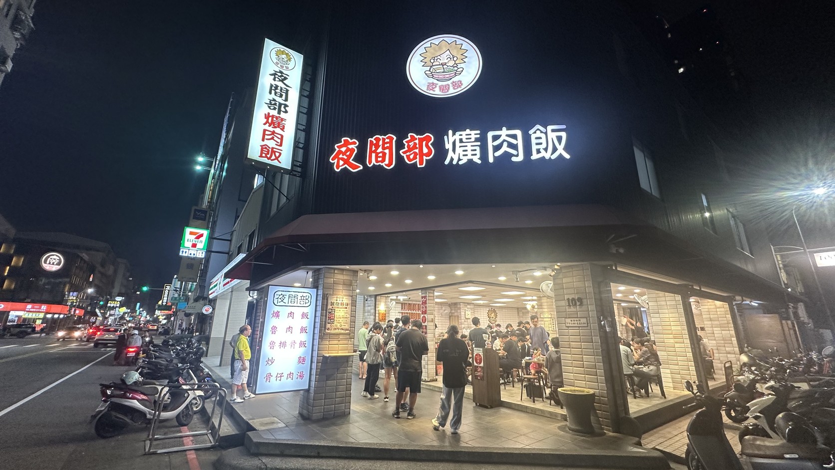 夜晚的夜間部爌肉飯轉角店面，黑色外牆、紅白發光招牌與門口候位的客人