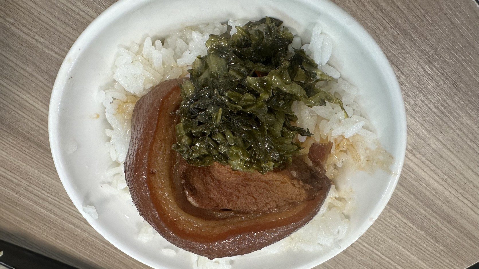 白色圓碗中的夜間部爌肉飯，一整塊彎曲的爌肉旁疊著深綠色酸菜