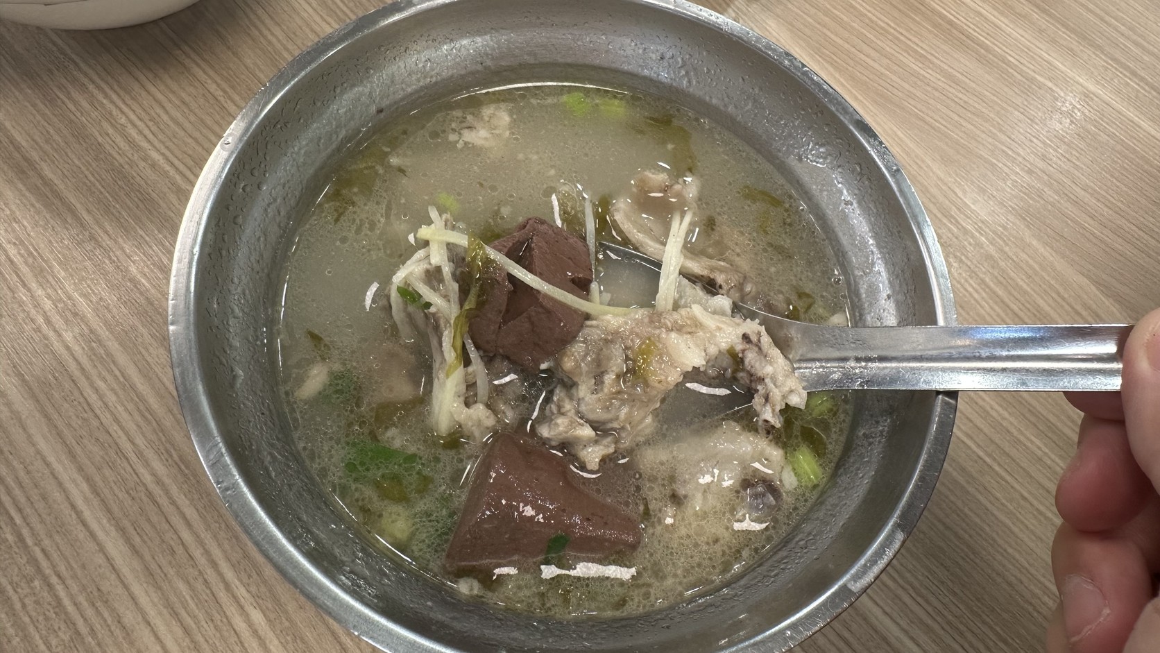 不鏽鋼碗裡的骨仔肉豬血湯，湯中有骨仔肉、兩塊豬血與蔥薑絲