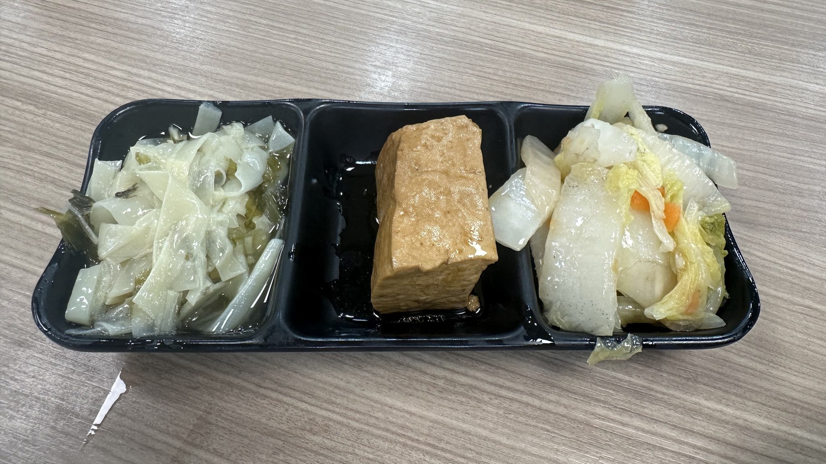 黑色三格小盤盛裝的三樣配菜，由左至右是竹筍、滷豆腐與白菜