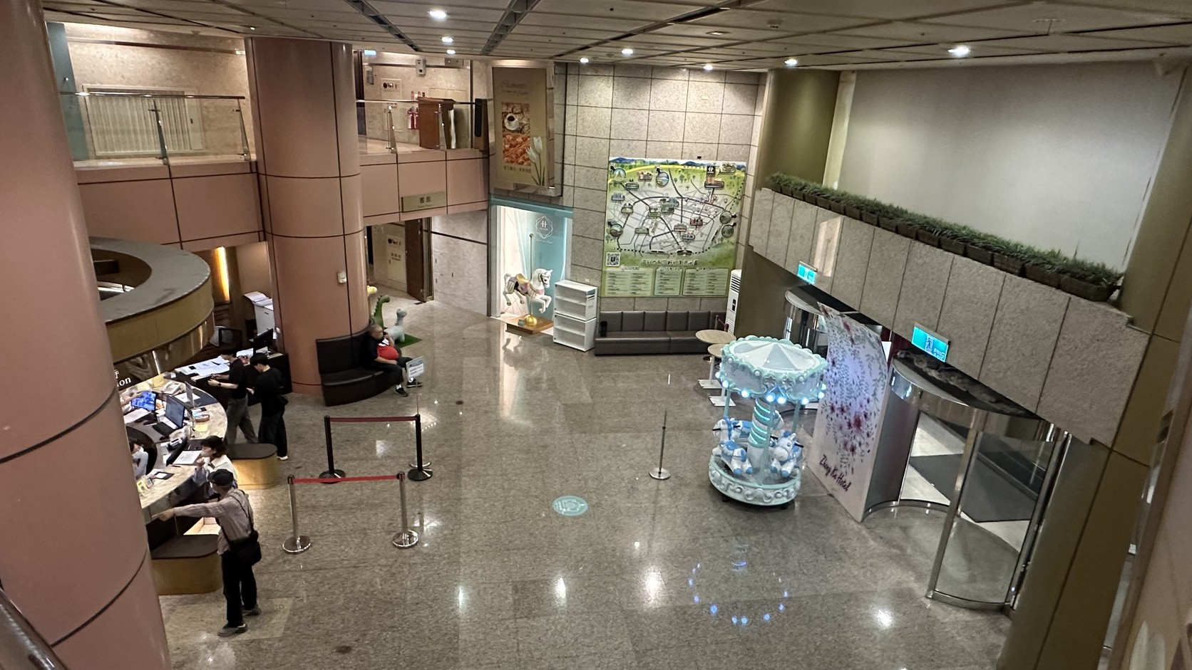 中科大飯店一樓挑高大廳：櫃檯、粉彩色旋轉木馬與牆上的輕旅美食地圖