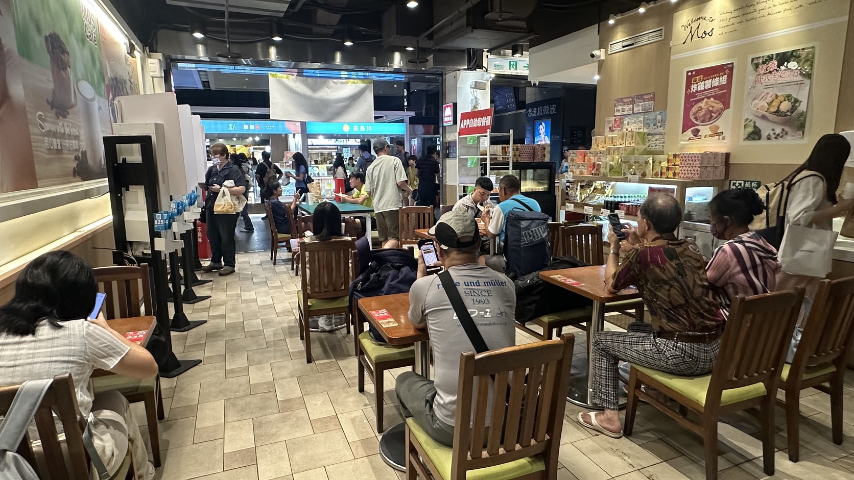 摩斯漢堡高鐵台中店內用區全景：木質桌椅、綠色坐墊與用餐客人