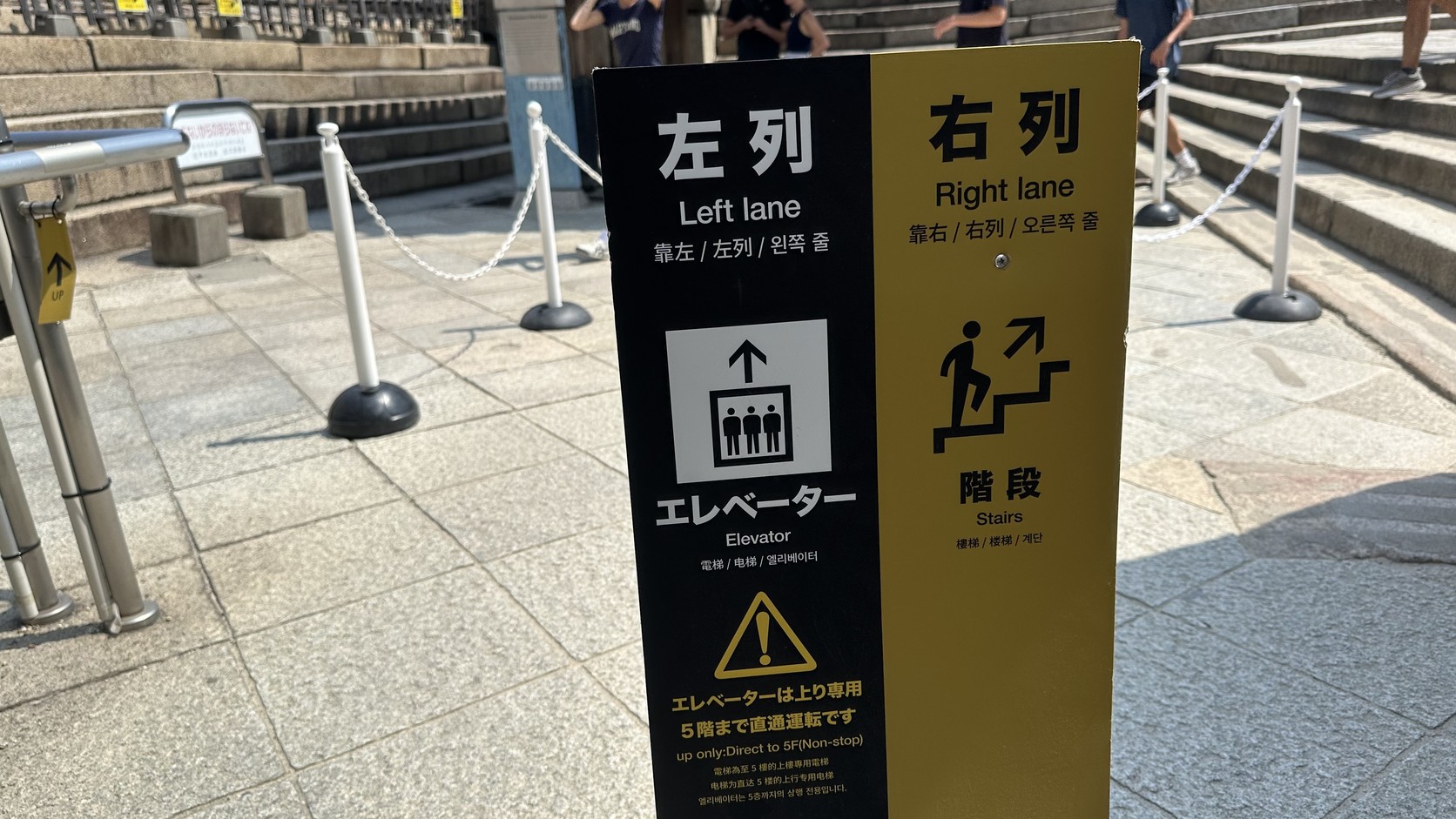 大阪城天守閣入口前的分流告示：左列為電梯、右列為樓梯，並標示電梯為上行專用、直達 5 樓