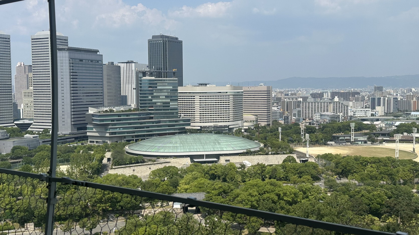 從八樓展望台望向遠方的大阪市區高樓群，前方是公園綠地與一座圓頂建築