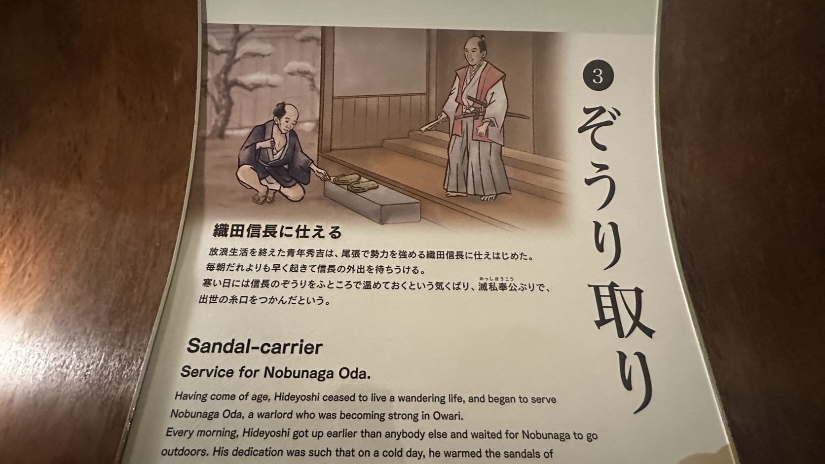 七樓「草履取り」展板，以日文與英文說明年輕的秀吉侍奉織田信長的故事，附有秀吉蹲著替信長溫熱草鞋的插畫