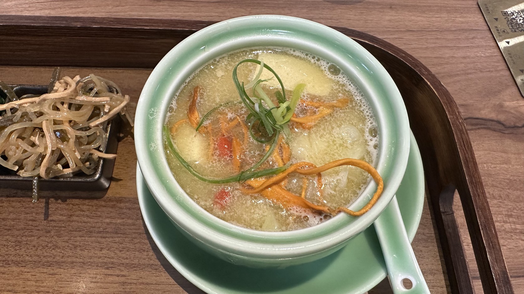 黃金清雞湯：青瓷湯碗裡有豆腐、白菜、蔥絲與橘紅色細長配料，湯面泛著細油花