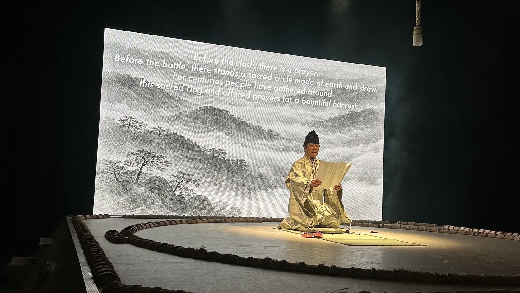 開場的祝禱儀式，穿著傳統服裝的人在土俵上朗讀，背後螢幕顯示英文文稿