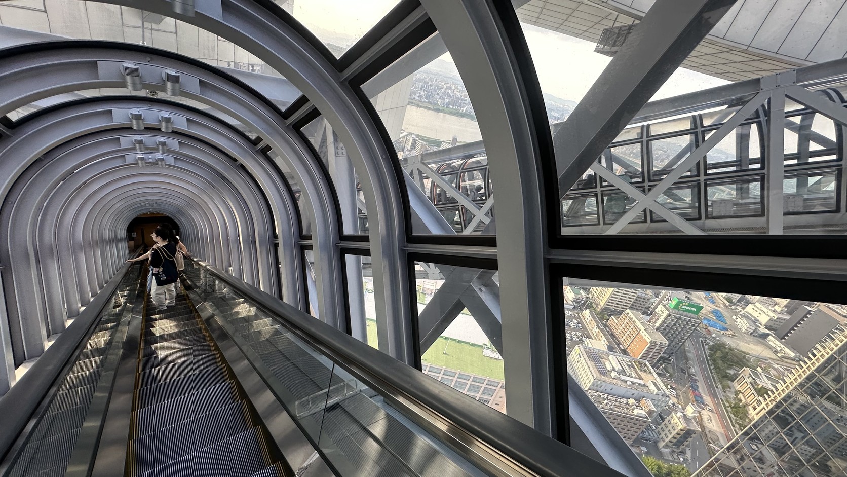 從空中手扶梯內向外看，粗大的鋼骨與窗外的城市景觀