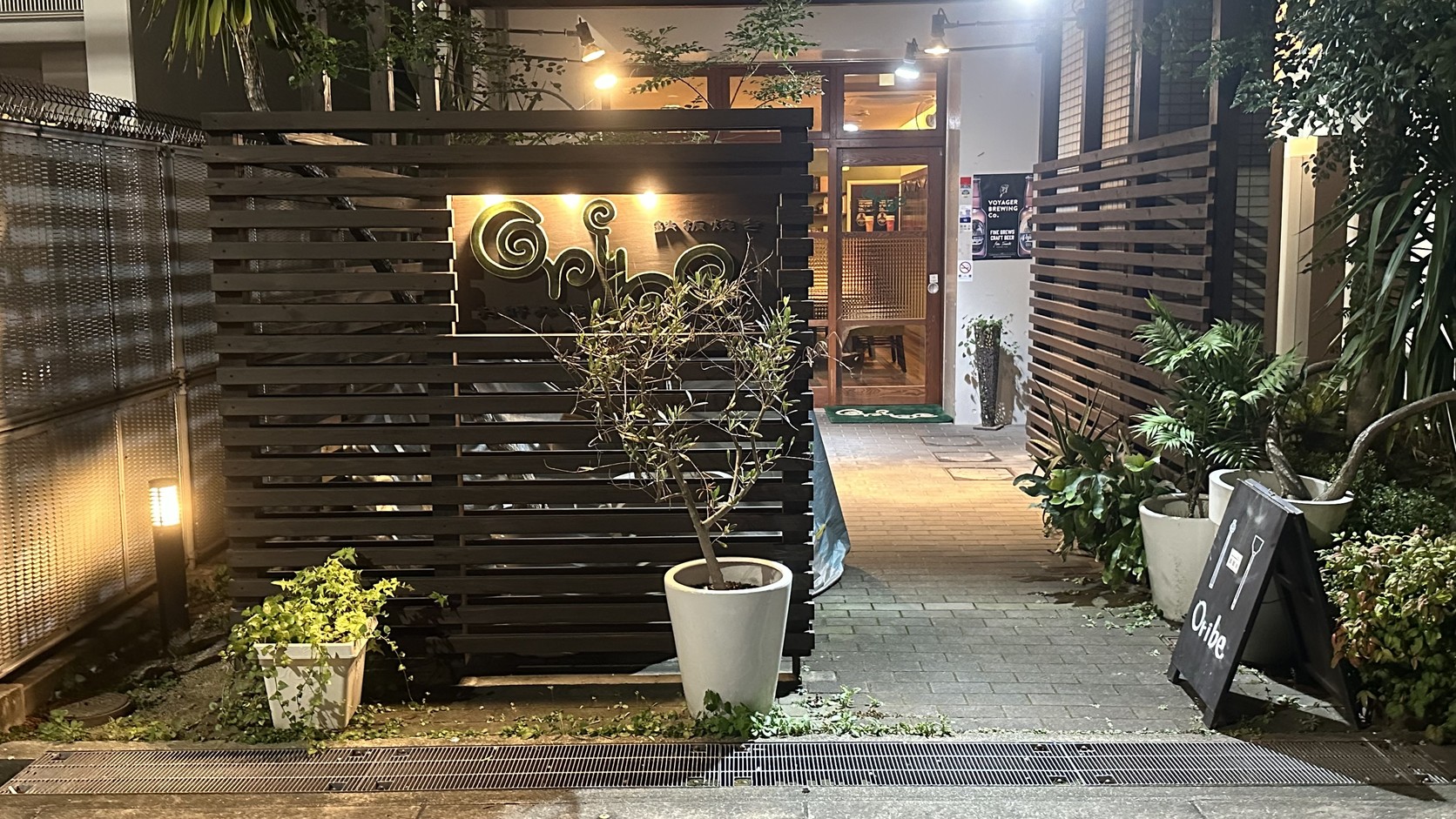 Oribe 夜間入口，木格柵招牌與立牌隱在植栽後方
