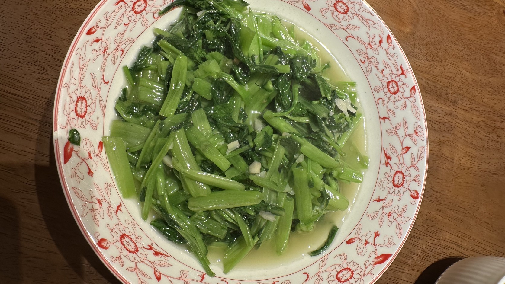 一大盤清炒空心菜，盛在紅色花紋的白瓷盤中