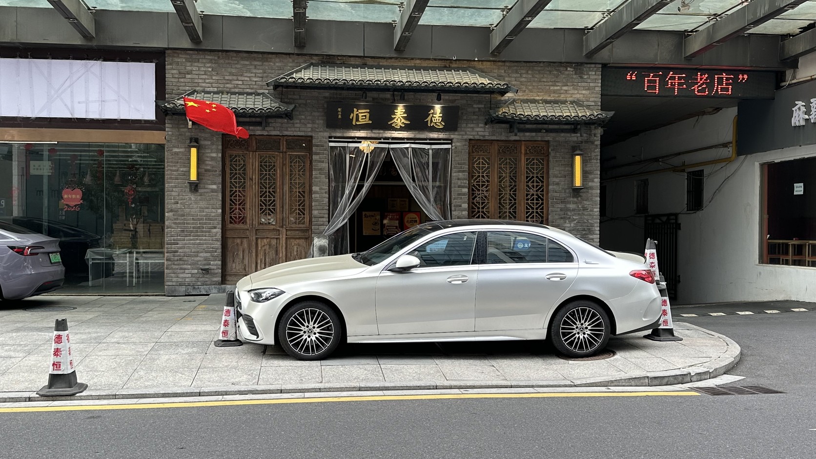 古典木門樓上掛著「德泰恒」匾額，門側亮著紅色的「百年老店」字樣，門前停著一輛白色轎車