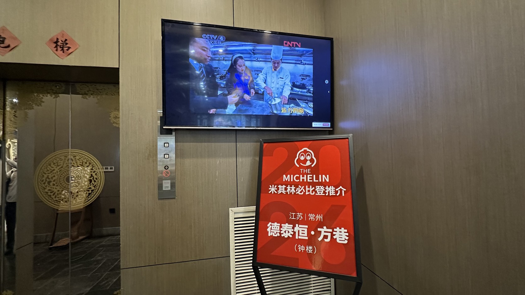 電梯旁的紅色立牌，印著 MICHELIN 必比登推介與「德泰恒·方巷（鐘樓）」字樣，後方牆上有一台電視