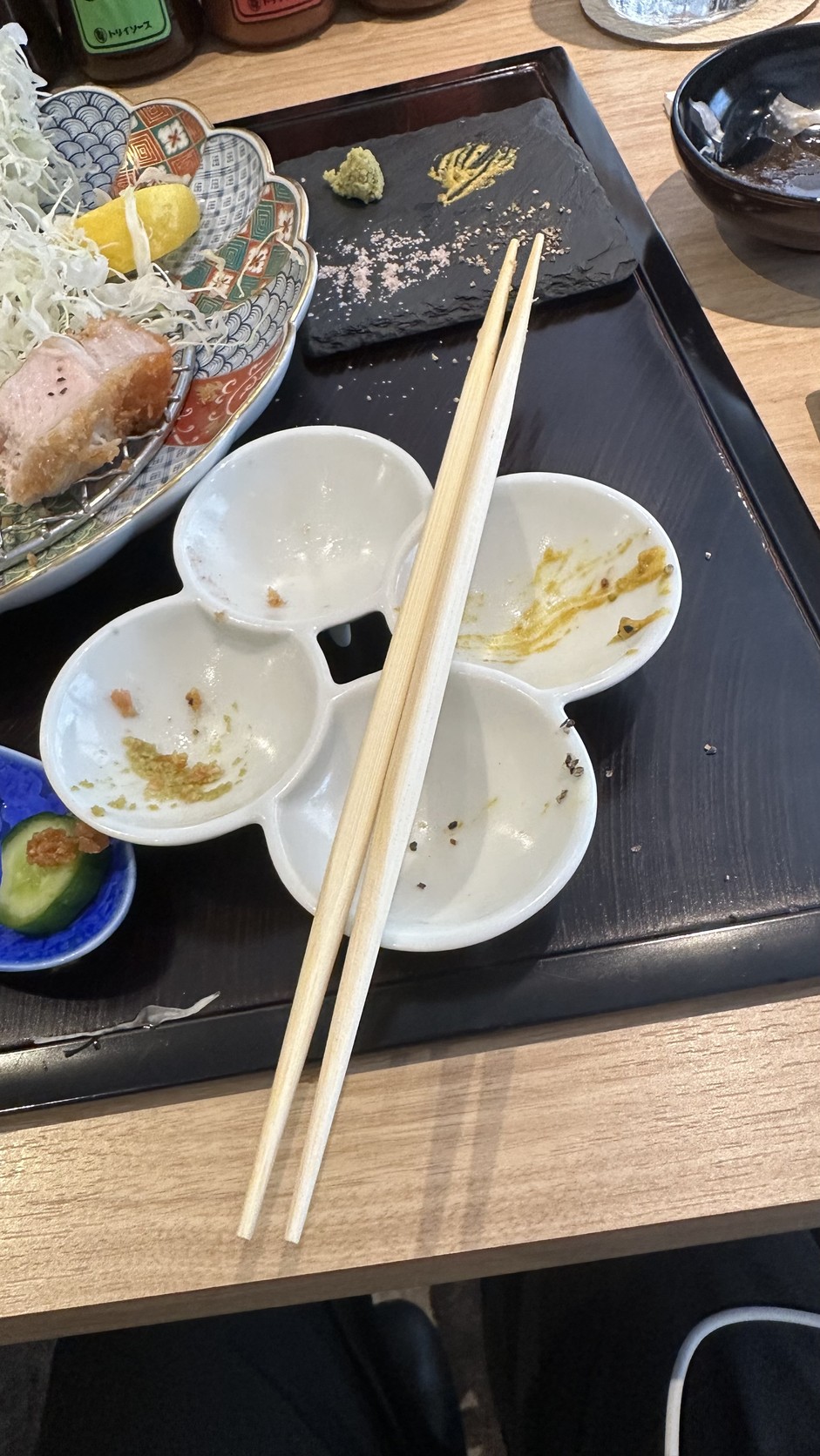 用餐後的四格小盤與筷子，各格殘留不同調味的痕跡，黑色石板上還有少量山葵、黃芥末與粉紅色的鹽