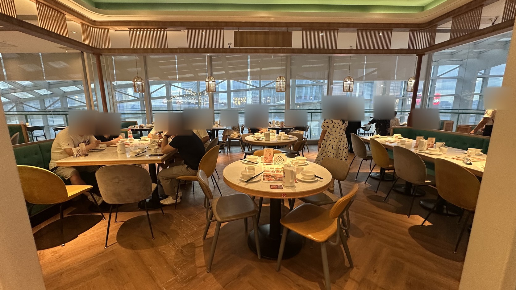 避風塘用餐大廳實拍，落地窗、木質地板、綠色沙發與圓桌，入鏡顧客的臉部已模糊